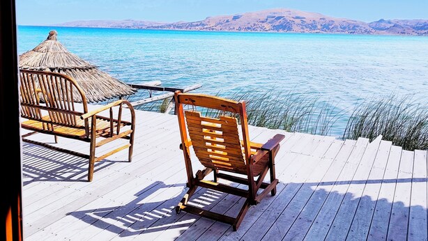 A wooden deck with two wooden chairs facing a calm sea and distant hills. - uros killa lodge (Puno)