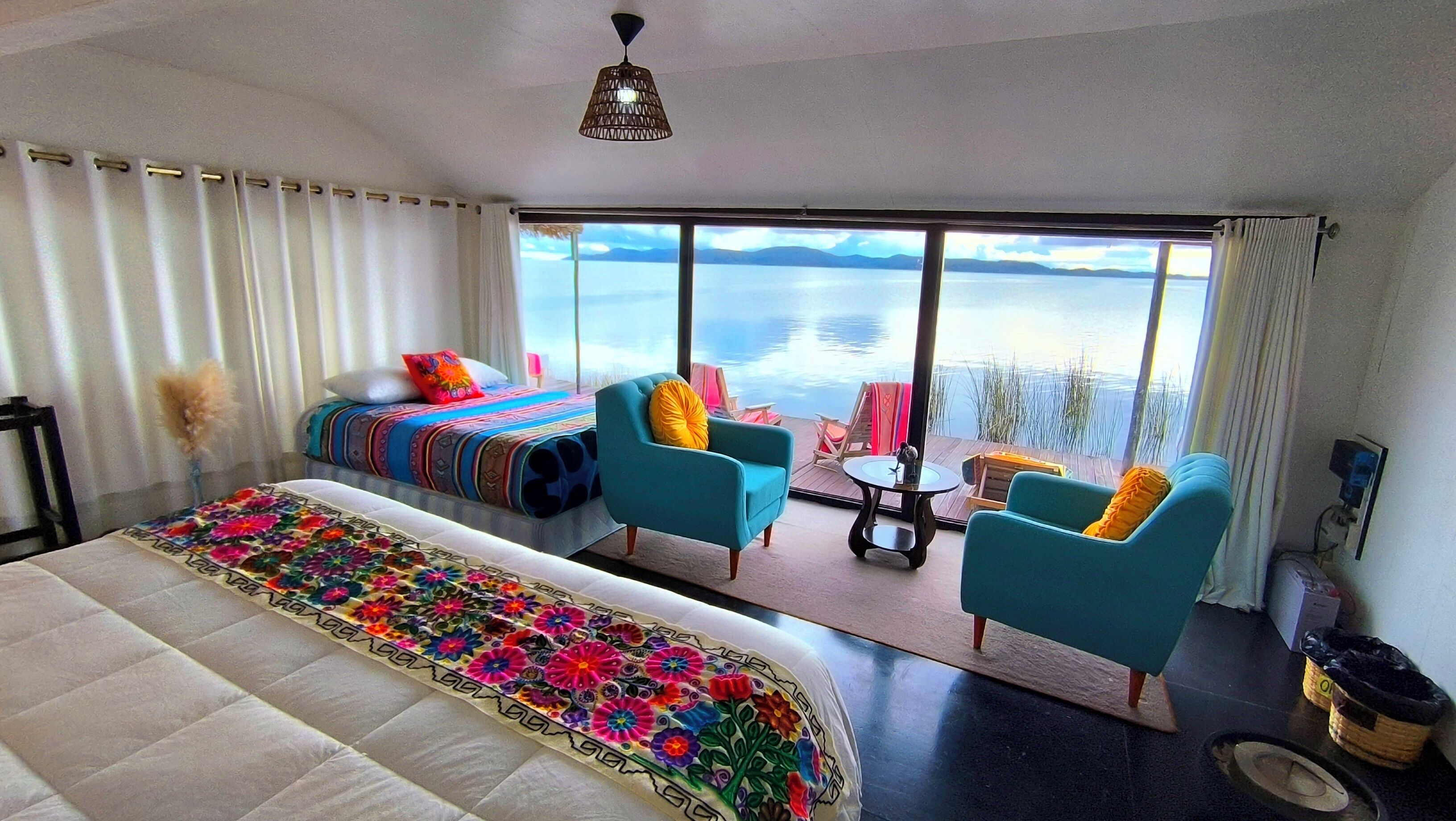 Une chambre avec un grand lit, deux fauteuils, une petite table et une vue sur l’eau.