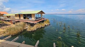 A lakeside wooden structure with a covered deck, a dock, and a view of the lake. - uros killa lodge (Puno)