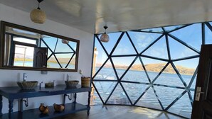A room with a large window, a wooden floor, a blue table with bowls, and a mirror. - uros killa lodge (Puno)
