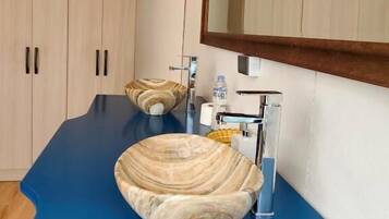 A bathroom with a blue countertop, a marble sink, a mirror, wooden cabinets, and two yellow pendant lights.