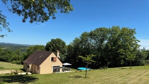 Ein Haus mit geneigtem Dach, einer Garage und einer kleinen Terrasse mit einem blauen Pool.