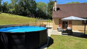 Ein Garten mit Swimmingpool, einer überdachten Terrasse und einem Haus mit Schornstein.