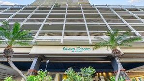 Um hotel imponente com vários varandas, palmeiras na frente e o nome 'Island Colony' na fachada.