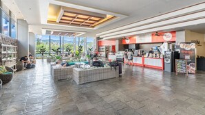 Um espaço amplo e interno com assentos, um balcão com cardápio e vista através de grandes janelas.