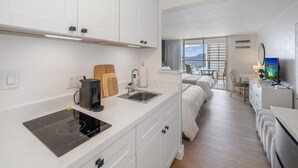 Quarto de hotel moderno com cozinha compacta, cama, escrivaninha e televisão.