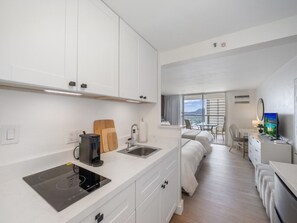 Ein modernes Hotelzimmer mit Küchenzeile, einem Bett, einem Schreibtisch und einem Fernseher.