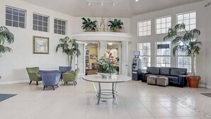A spacious lobby with a central round table, seating area with sofas, potted plants, and a vending machine.