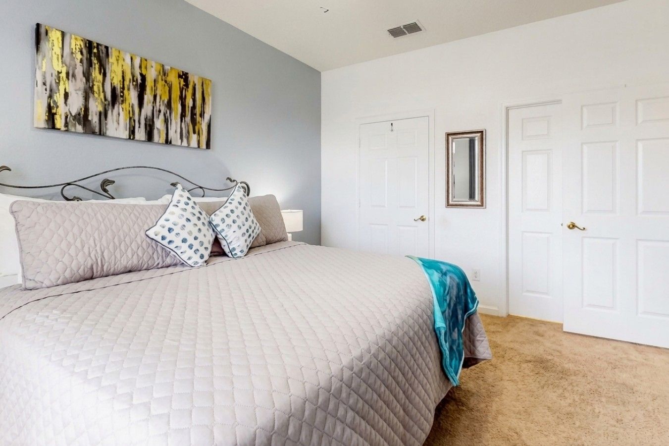A bedroom with a bed, a nightstand, a wall-mounted mirror, and a door.