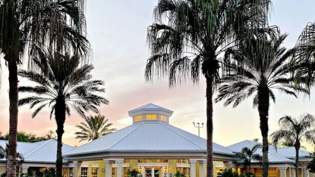 A hotel with a central dome structure, palm trees, and a well-maintained garden.