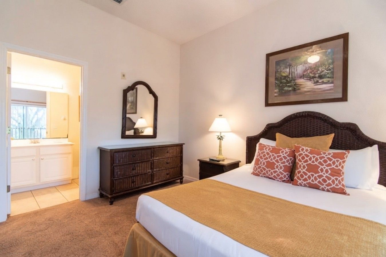 A bedroom with a bed, dresser, nightstand, lamp, and a painting on the wall.