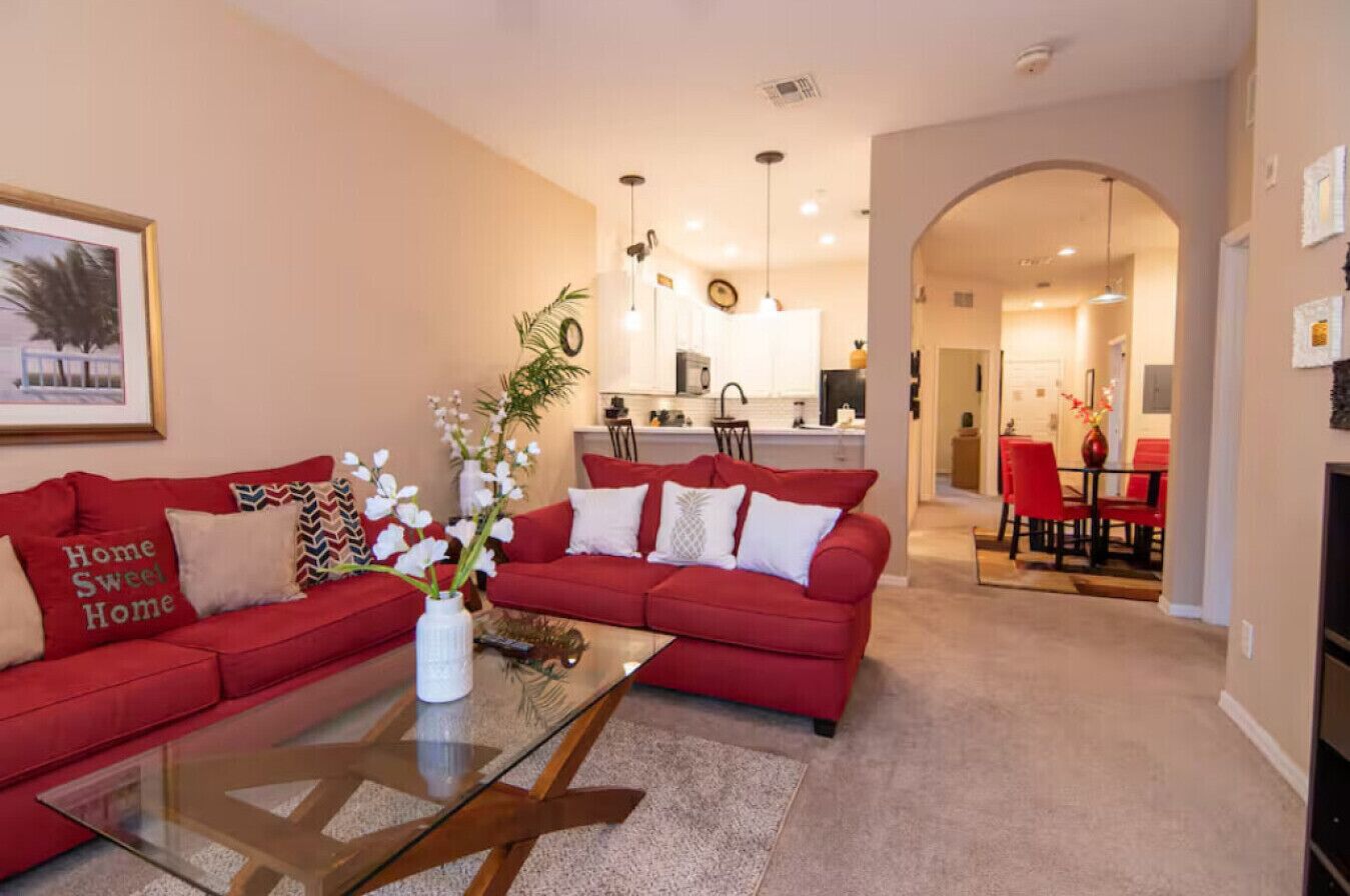 Ein Wohnzimmer mit einem roten Sofa, einem Glastisch und einer Küche im Hintergrund.