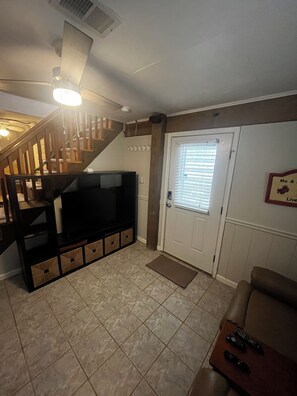 A living room with a TV, wooden staircase, and a door with blinds. - Short Walk To Beach-Between Highways-Near Avalon Pier- Hot Tub (Kill Devil Hills)
