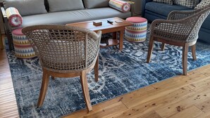 En stue med sofa, to fletstole, et sofabord, et mønstret tæppe og et billede på væggen.