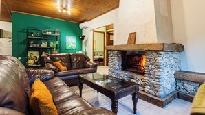 A living room with a stone fireplace, leather sofas, and a green accent wall. - Taygetos Relaxing Cottage (Poliani)