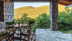 A stone patio with a table and chairs, a view of a mountain, and a wooden ceiling. - Taygetos Relaxing Cottage (Poliani)