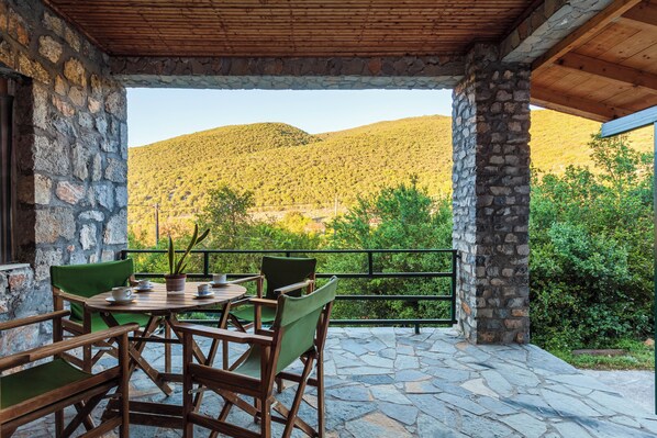 A stone patio with a table and chairs, a view of a mountain, and a wooden ceiling.