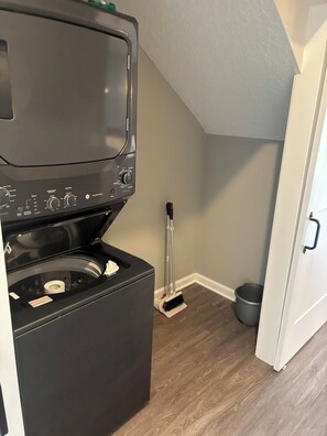 A compact washer and dryer unit in a small laundry room with a mop and bucket. - Keefer Creek A106 (Dogs Welcome!) (Fort Wayne)