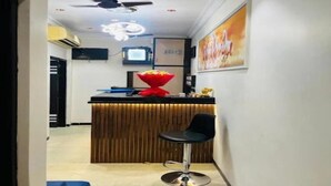 A reception area with a wooden counter, a black office chair, a ceiling fan, and a television mounted on the wall. - Hotel Blue Sunrise near Mumbai Airport (Mumbai)