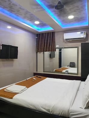 A hotel room with a bed, a mirror, an air conditioning unit, and a ceiling with blue lighting.
