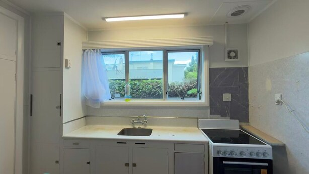 A compact kitchen with a window, a sink, a stove, and cabinets. - 3 bedroom house (Rotorua)