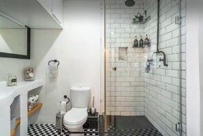 Un baño con inodoro, lavamanos, espejo, ducha y suelo a cuadros.
