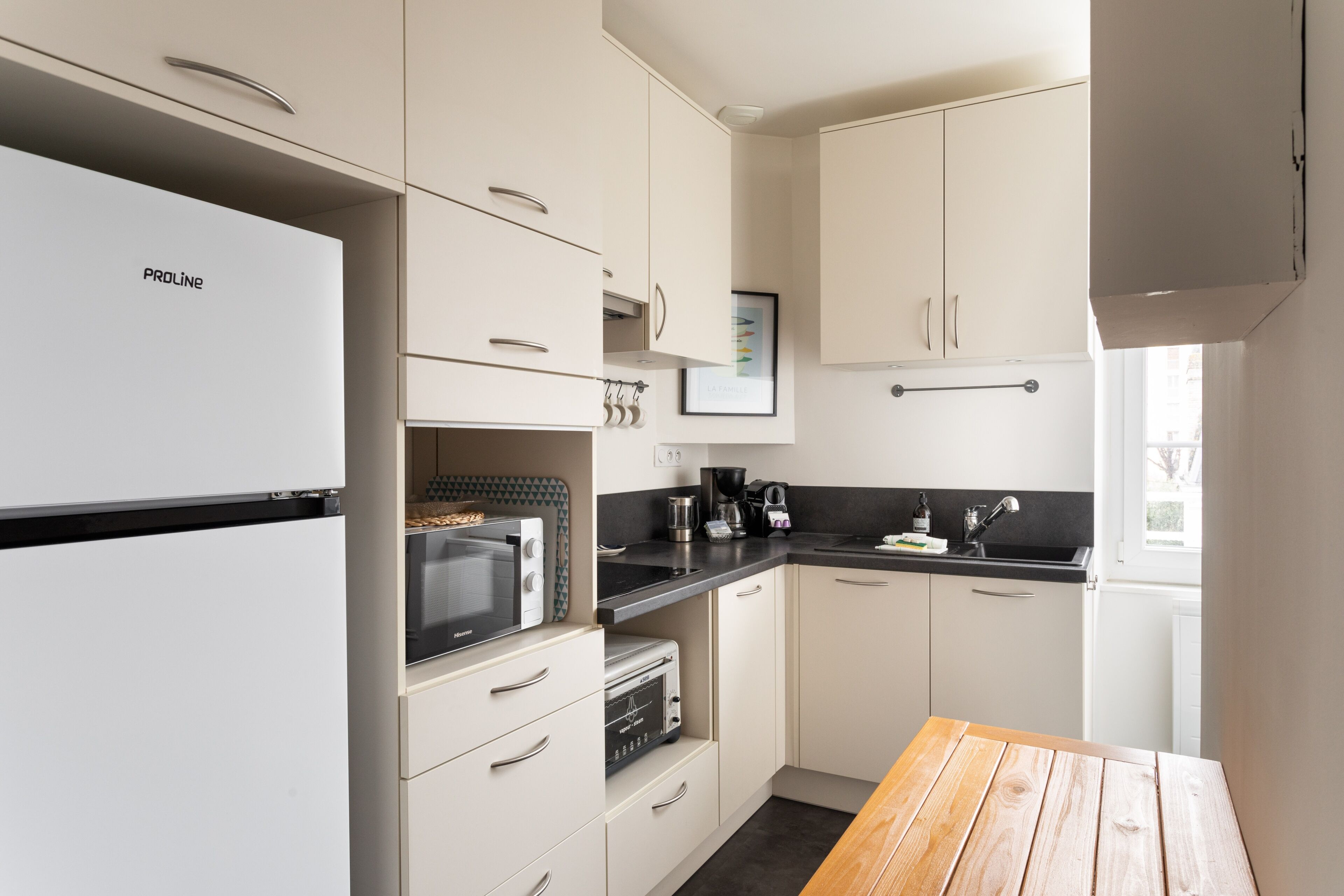 Eine moderne Küche mit weißen Schränken, einem ProLine-Kühlschrank, einer Mikrowelle, einer Kaffeemaschine und einem Holztisch.