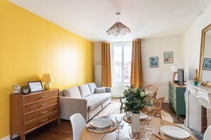 Ein Wohnzimmer mit einer Couch, einem Esstisch gedeckt mit Tellern und Gläsern, einer Holzkommode und einem Spiegel.