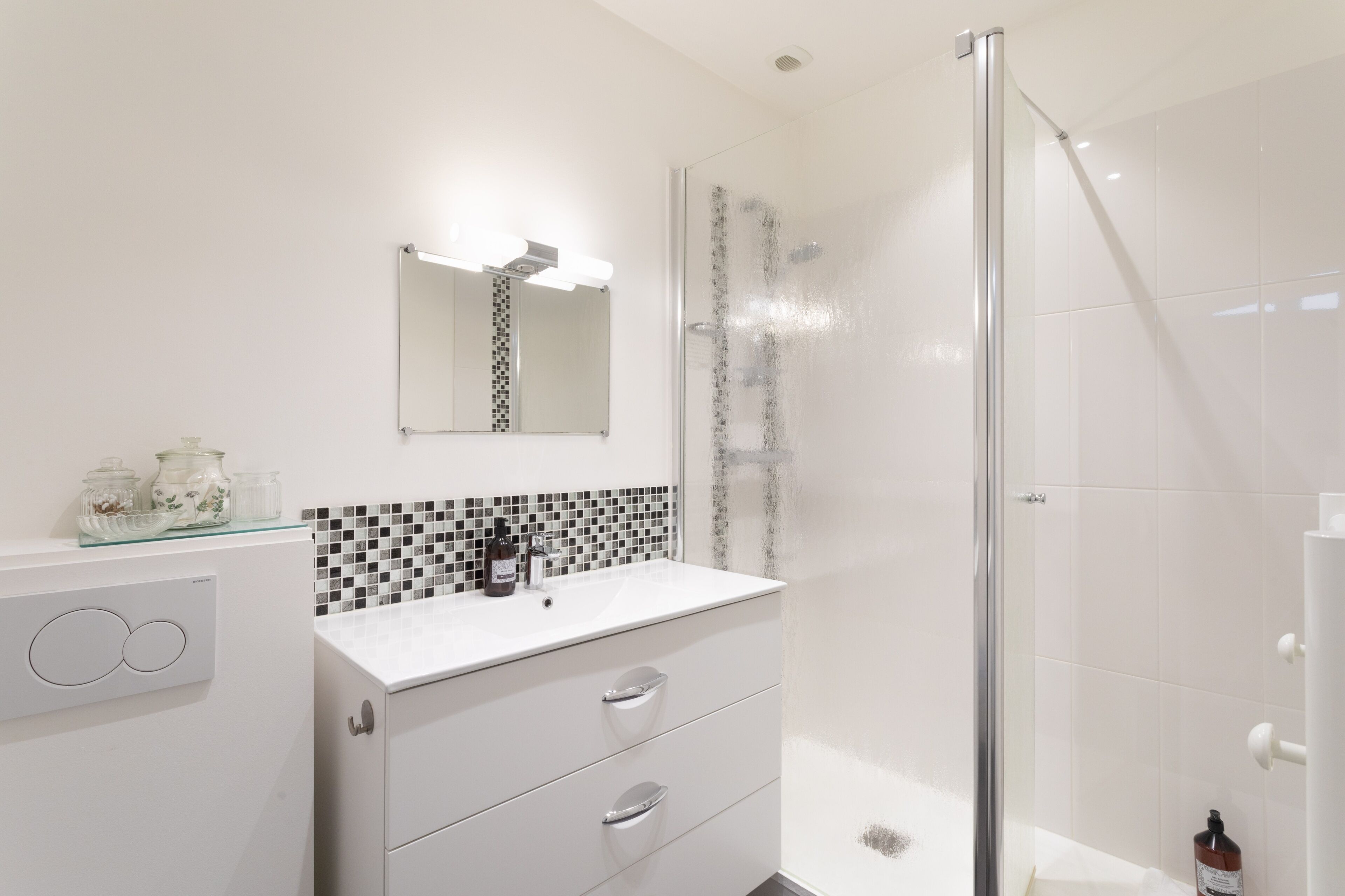 A modern bathroom with a glass shower enclosure, a white vanity with a mirror, and a tiled backsplash.