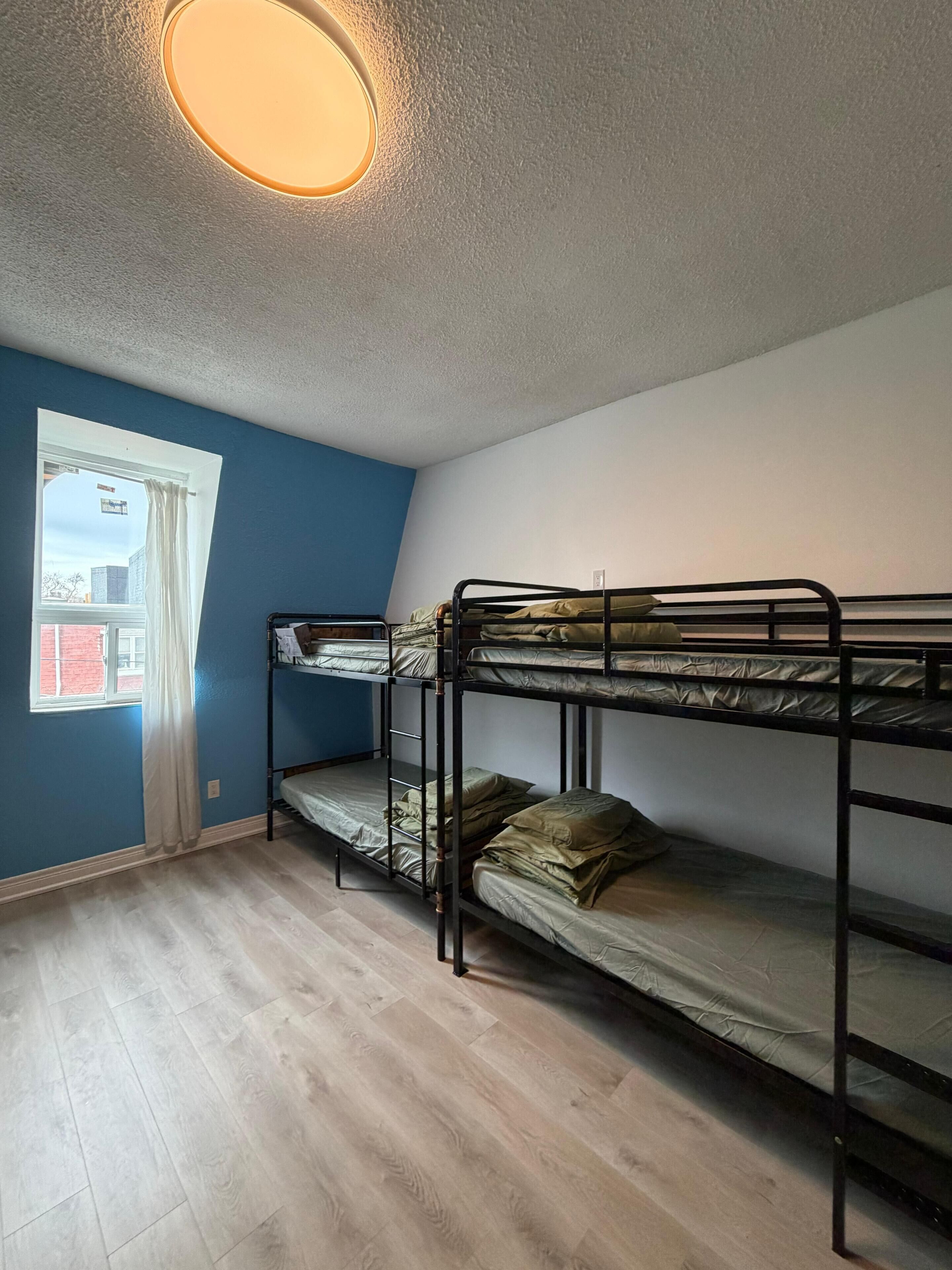 Une chambre avec des lits superposés, une fenêtre avec des rideaux et un luminaire au plafond.