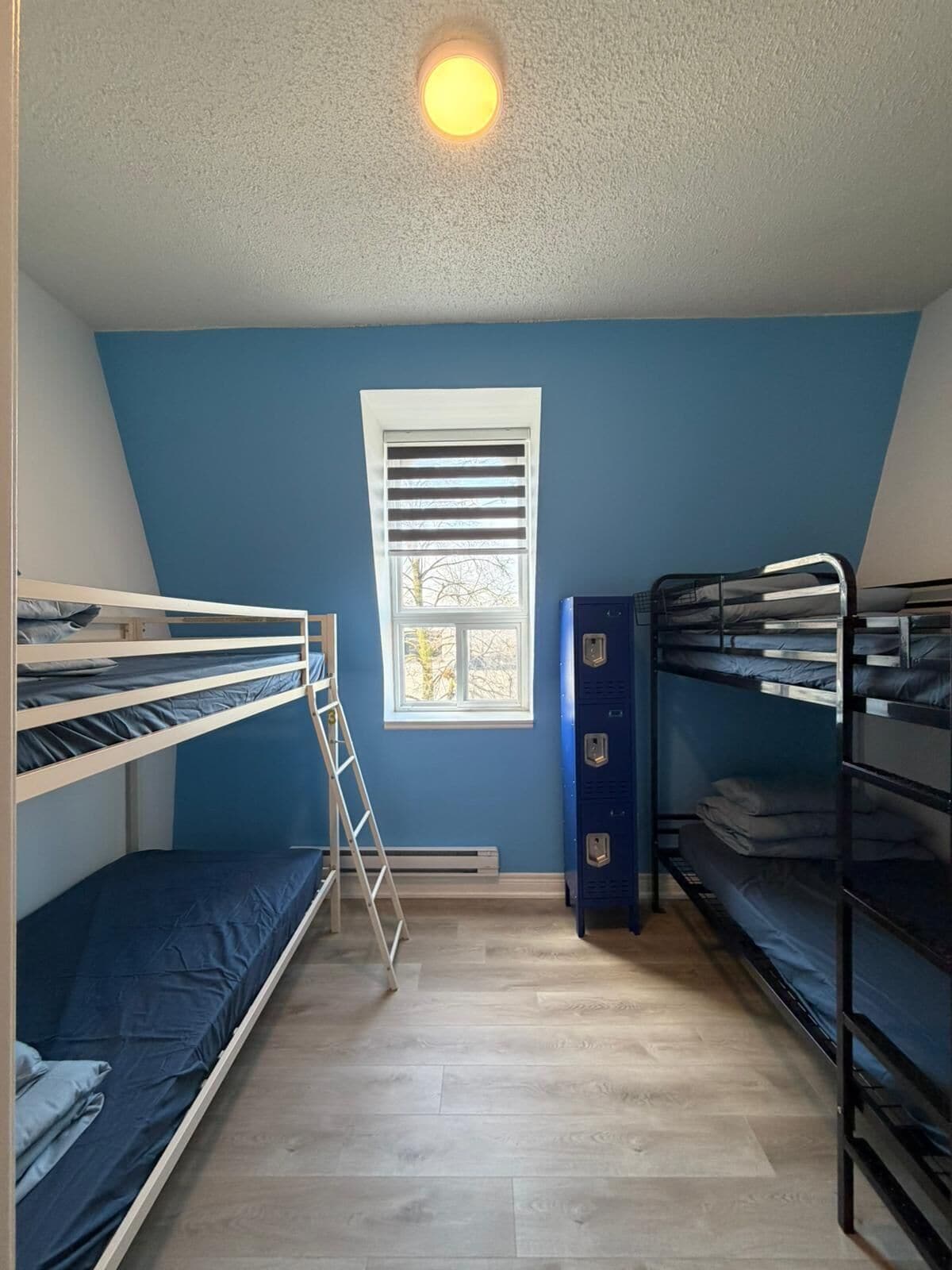 A dormitory room with bunk beds, a window, and a ceiling light.