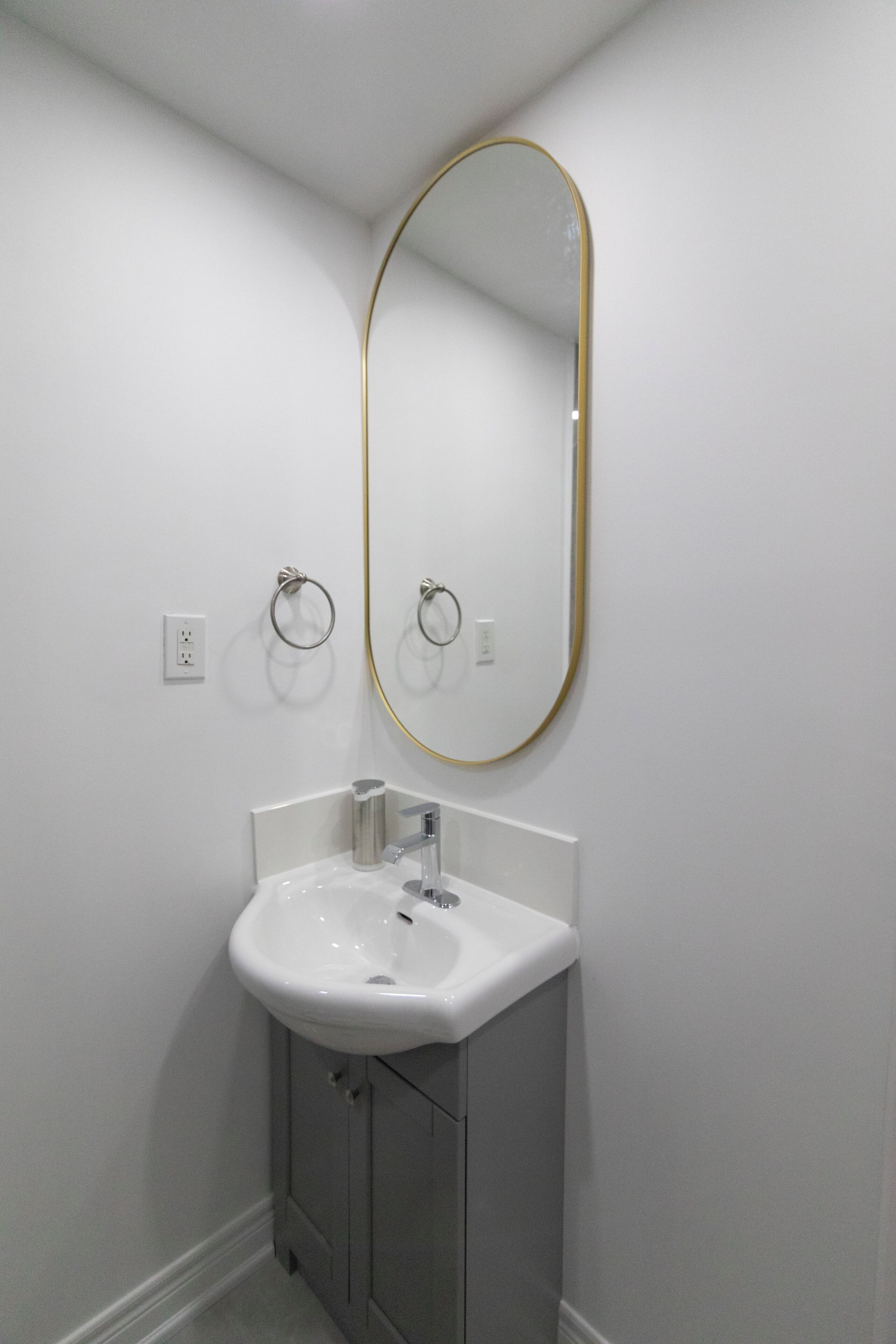 A bathroom with a white sink, a gold-framed mirror, and a towel ring.