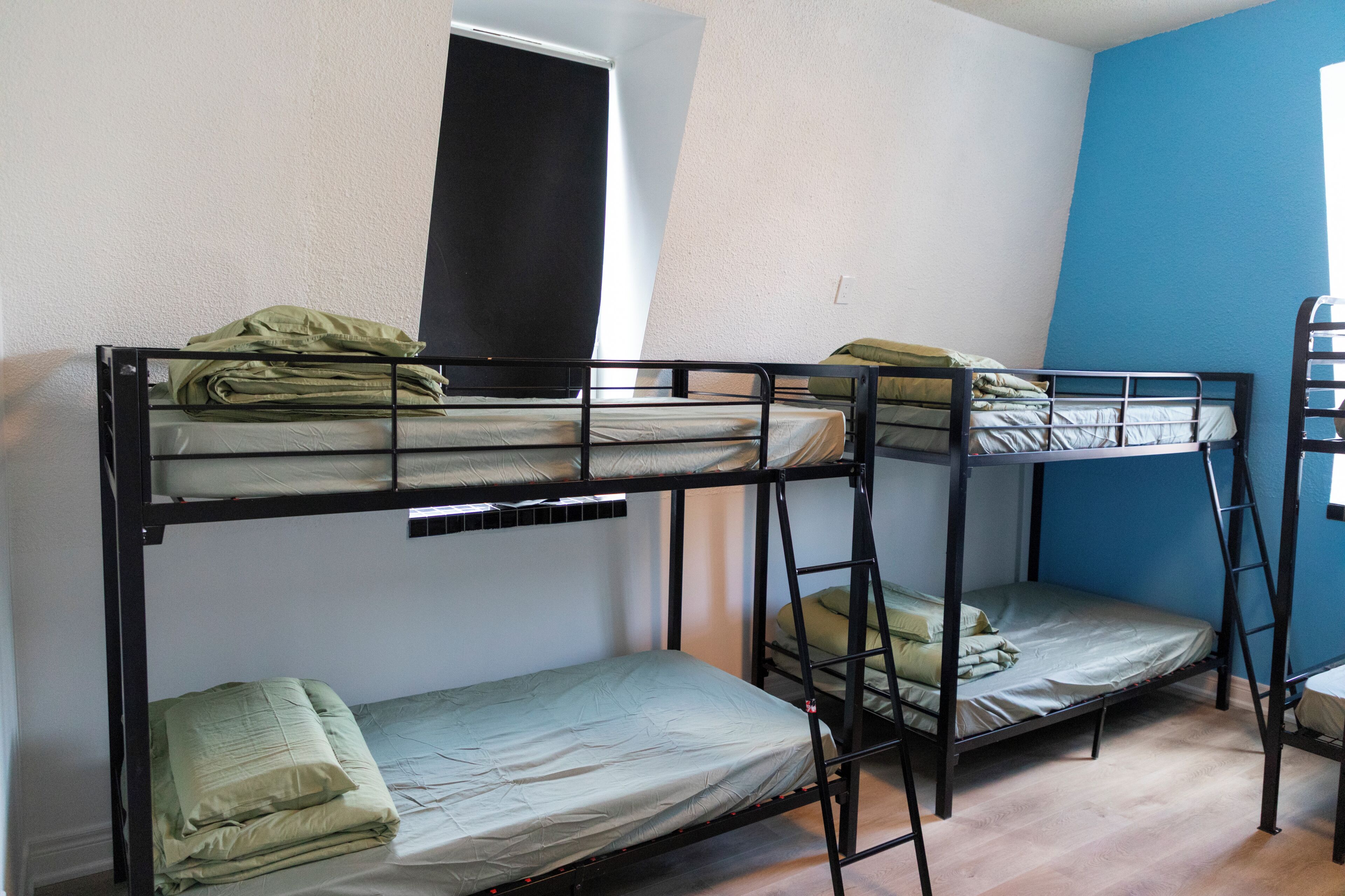 A dormitory room with bunk beds, a window, and a blue wall.