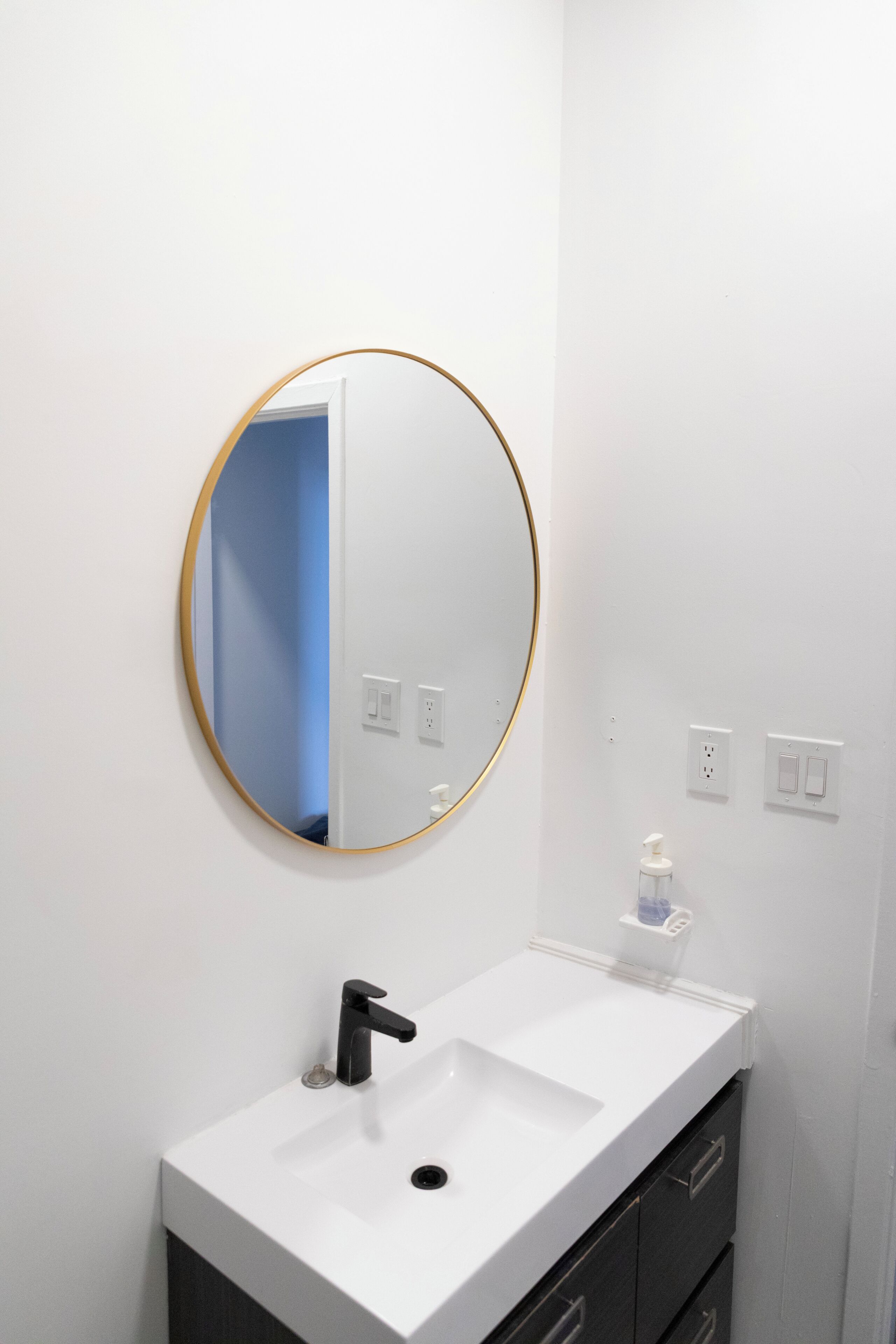 A bathroom with a white sink, a round mirror with a gold frame, and a blue door in the background.