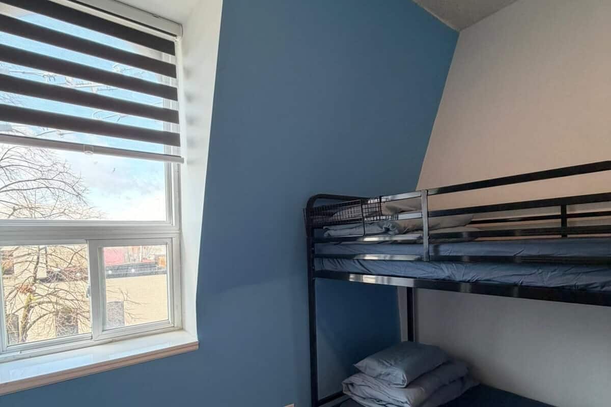 Une chambre avec un lit superposé, une fenêtre, un plancher en bois et un radiateur mural.