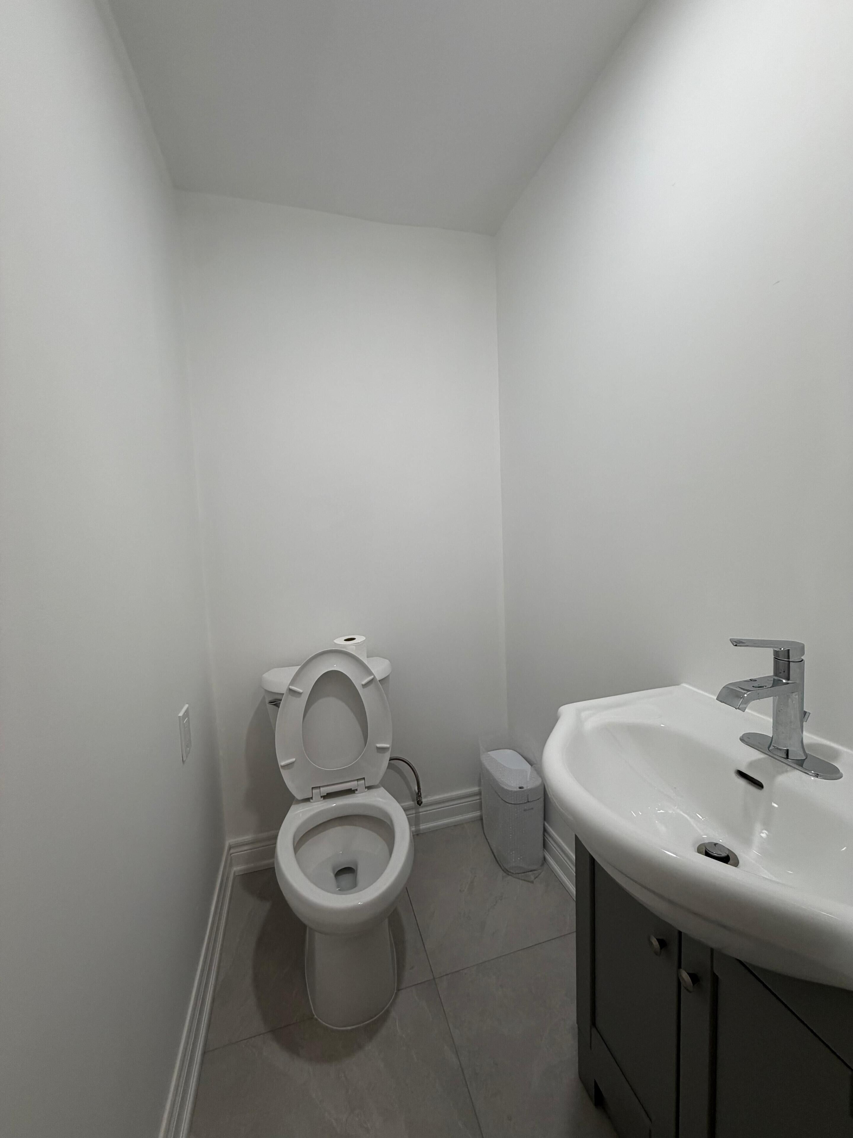 A bathroom with a toilet, sink, and trash can.
