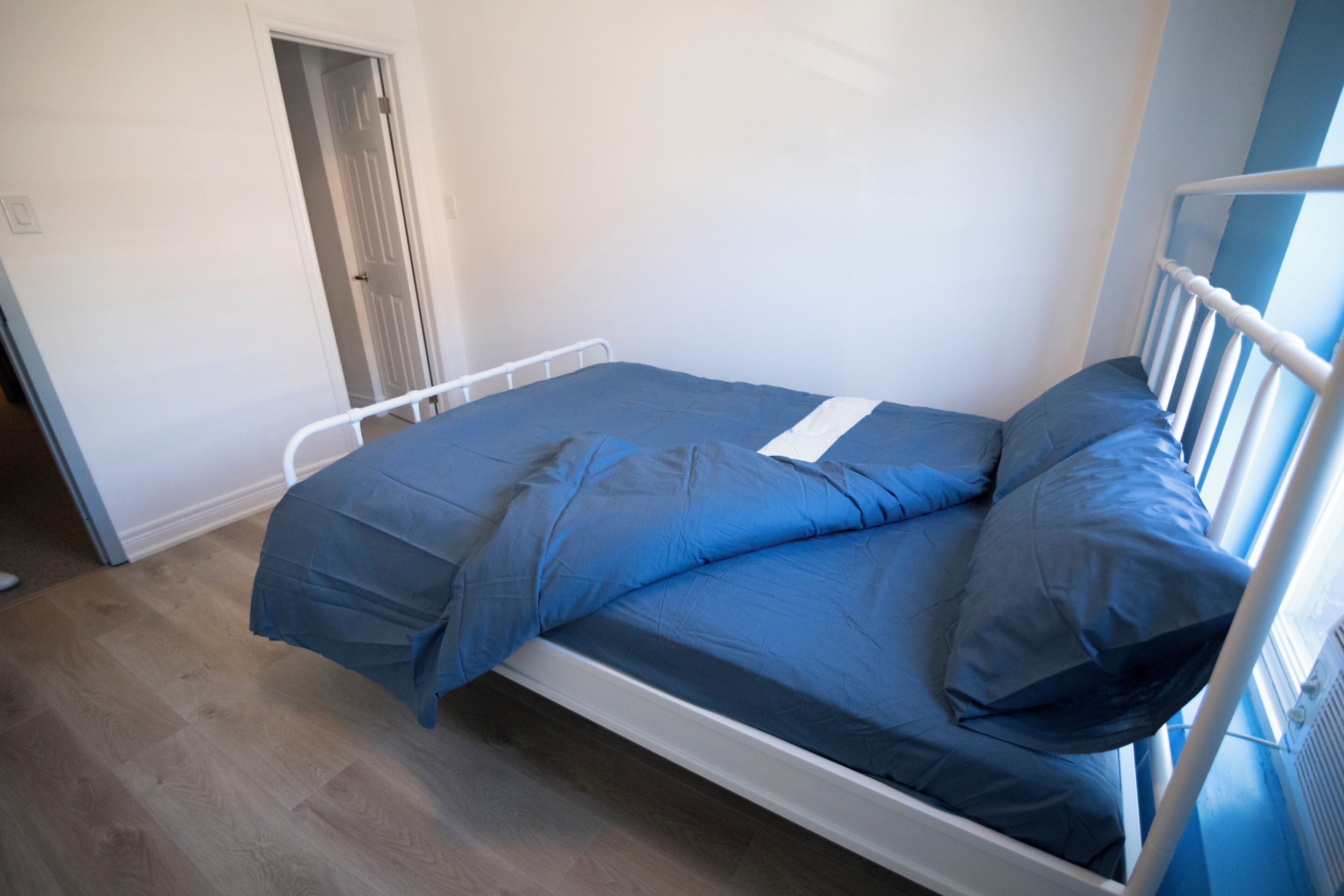 A single bed with a white metal frame, a blue mattress, and matching pillows.