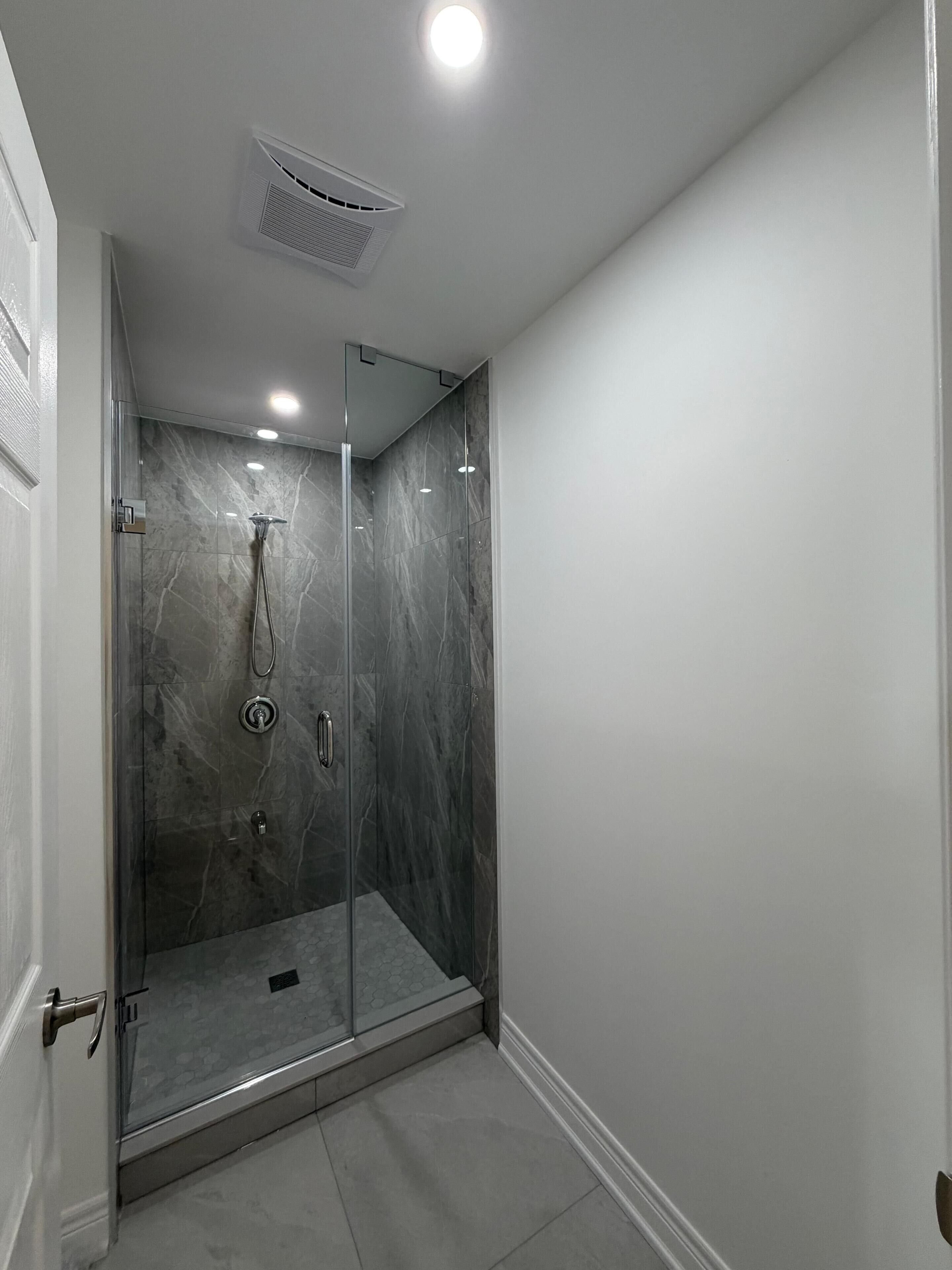 A modern bathroom with a glass-enclosed shower, marble walls, and a recessed ceiling light.