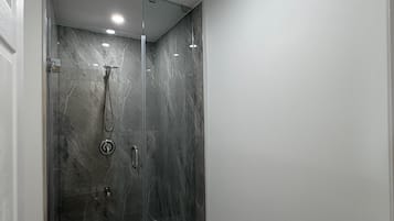 A modern bathroom with a glass-enclosed shower, marble walls, and a recessed ceiling light.