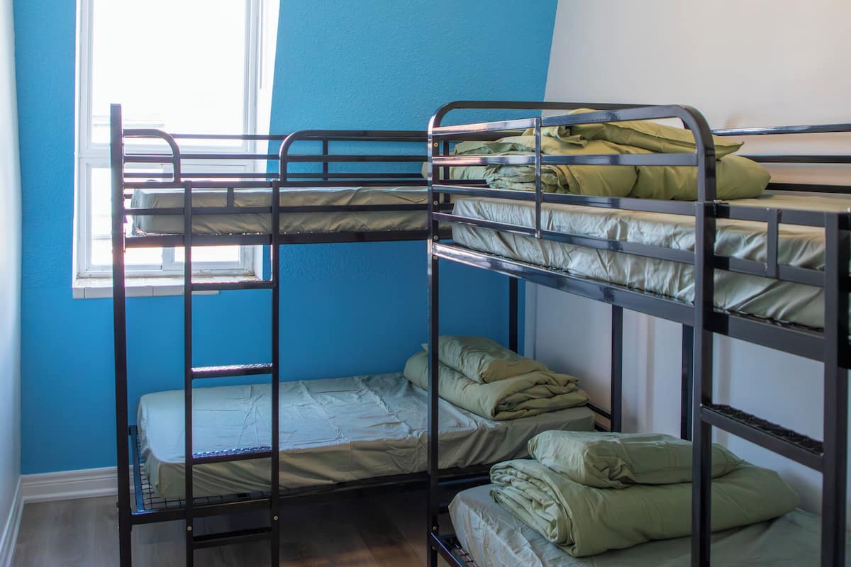 Une chambre avec un lit superposé, une fenêtre, un plancher en bois et un luminaire au plafond.