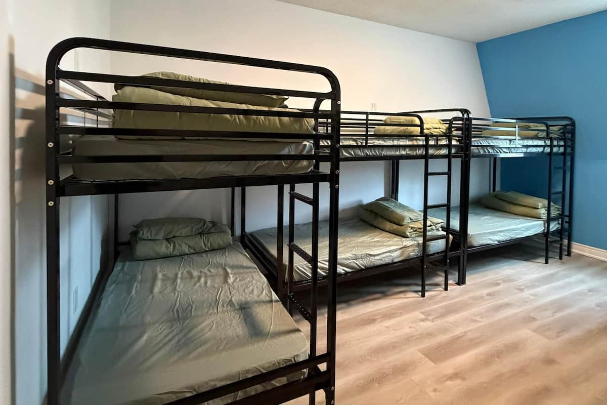 Une chambre de dortoir avec des lits superposés, un plancher en bois et un luminaire au plafond.