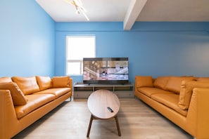 Un salon avec deux canapés en cuir, une table basse ronde en bois, un téléviseur à écran plat et une fenêtre.