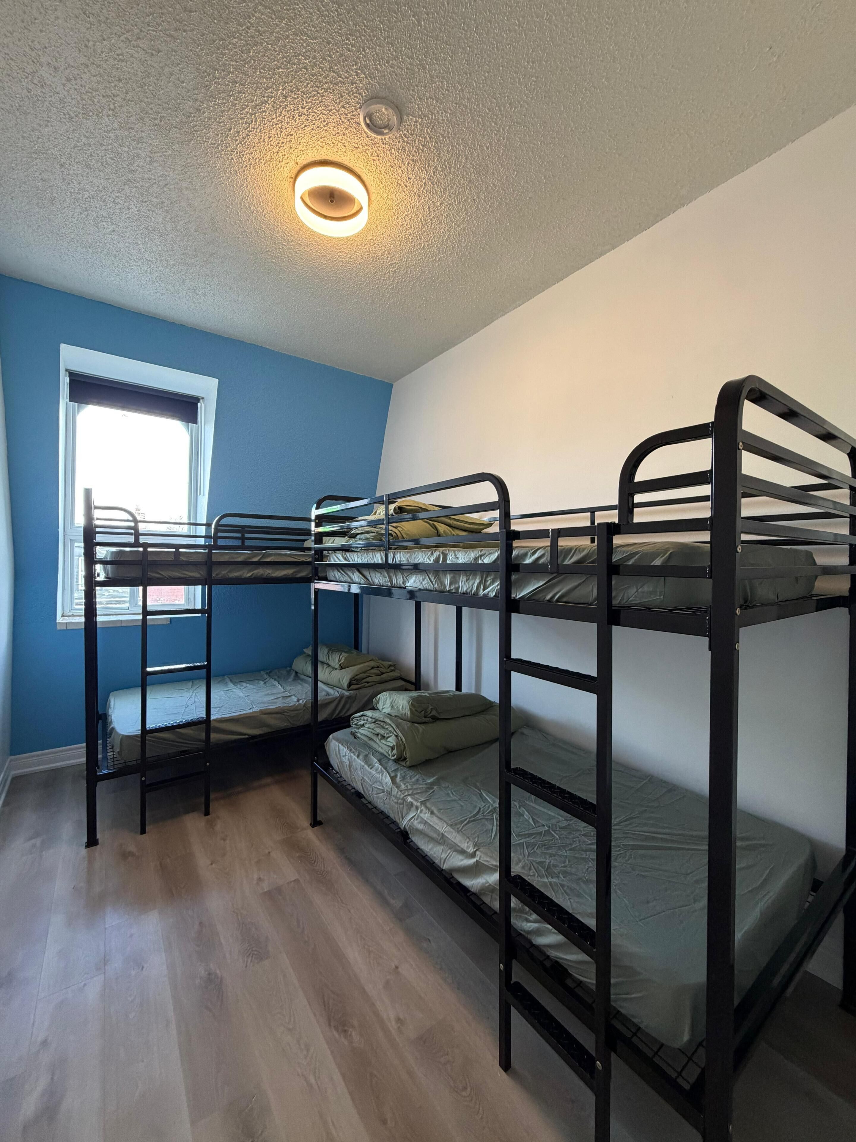 A bunk bed room with a window, a ceiling light, and wooden flooring.