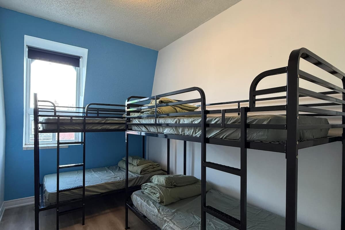 Une chambre avec un lit superposé, une fenêtre, un luminaire au plafond et un plancher en bois.