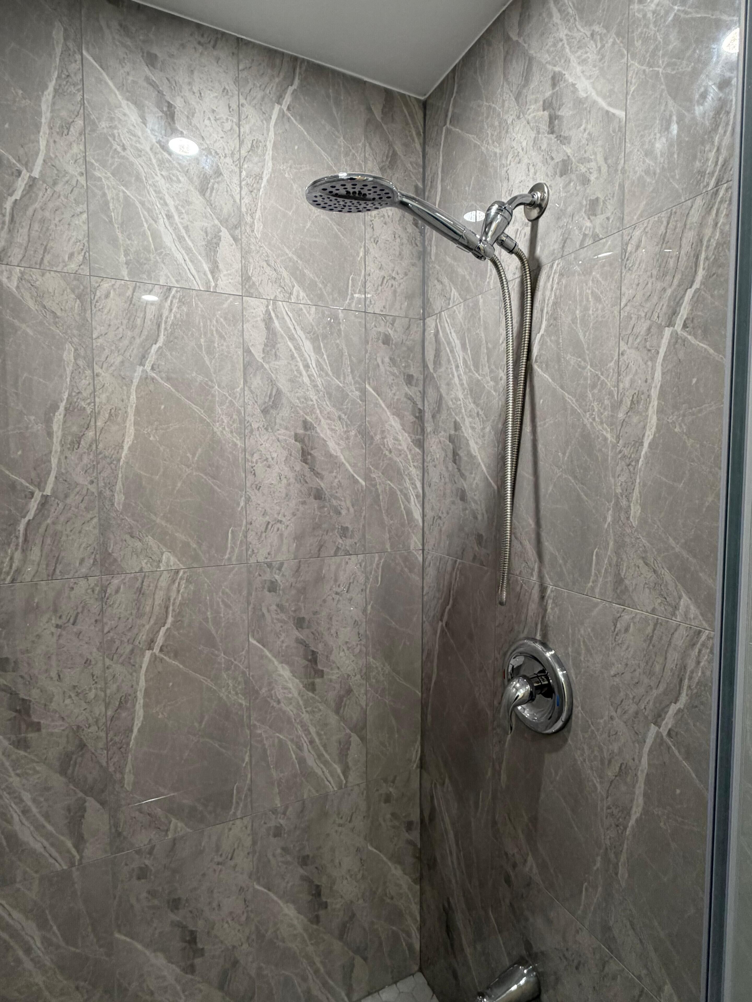 Ducha con cabezal de ducha de mano y grifo empotrado en una pared de mármol.