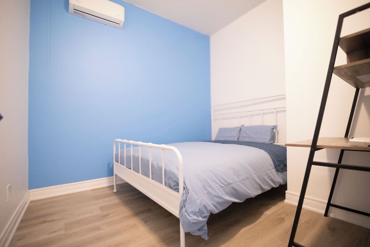 Une chambre à coucher avec un lit, un climatiseur blanc, un mur bleu et un plancher en bois.