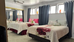 Hotellihuone, jossa on kaksi sänkyä, kattotuuletin, ikkuna verhoilla ja matolla peitetty lattia.