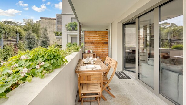 A modern outdoor dining area with a wooden table and chairs, a glass railing, and a view of the surrounding greenery. - L'Harona - Proche de la gare et du métro (Toulouse)