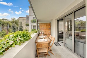 Ein moderner Essbereich im Freien mit Holztisch und -stühlen, einer Glasumlaufung und Blick auf die umliegende Bepflanzung.