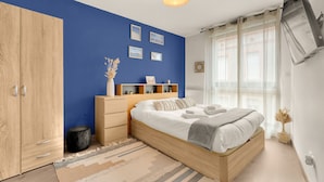 A bedroom with a bed, a wardrobe, a bedside table, a lamp, and a window with curtains. - L'Harona - Proche de la gare et du métro (Toulouse)
